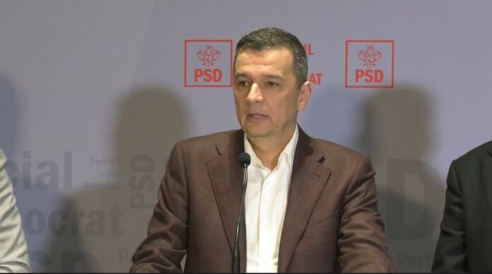Sorin Grindeanu, politician PSD, la masa de sedinta intr-o sala oficiala cu alti demnitari. Costum bleumarin inchis, camasa alba fara cravata. Privire serioasa, concentrata. Mai multi oficiali vizibil