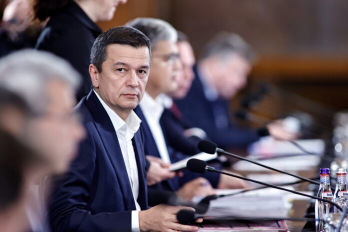 Sorin Grindeanu la ședință guvernamentală, costum cu cămașă albă, privire concentrată, alți miniștri în fundal