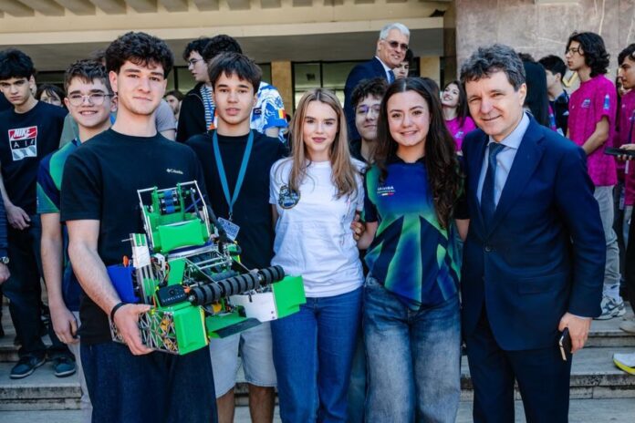 Nicusor Dan la masa de conferinta internationala, vorbind la microfon cu gest explicativ. Costum bleumarin, insigna. Placa 'ROMANIA' in fata. In spate, alt delegat. Fundal albastru de summit. Atmosfer